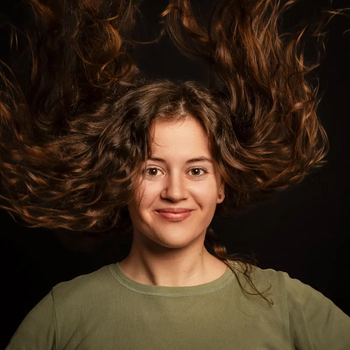 Junge Frau mit nach oben fliegenden Locken und leichtem Lächeln vor schwarzem Hintergrund – Studioportrait Soest