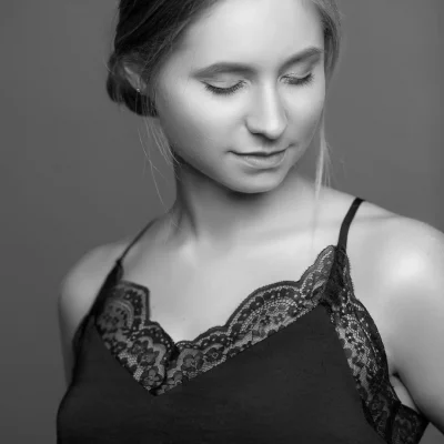 Junge Frau mit geschlossenen Augen, seitlich abgewandt, in schwarzem Top mit Spitzenbesatz, schwarz-weiß aufgenommen
