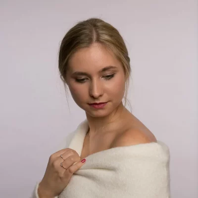 Lisa-Carolina mit locker über die Schultern gezogenem, weißem Pullover vor neutralem Hintergrund