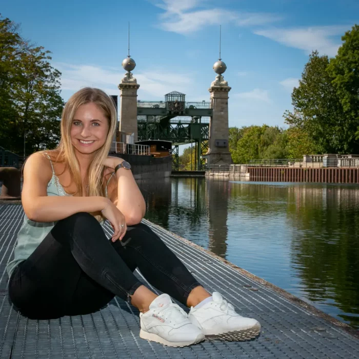 Lisa-Carolina, sitzend auf einem Steg vor dem historischen Schiffshebewerk, inmitten grüner Bäume und blauem Wasser