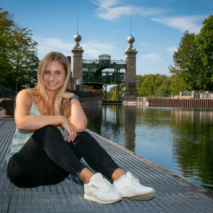 Lisa-Carolina, sitzend auf einem Steg vor dem historischen Schiffshebewerk, inmitten grüner Bäume und blauem Wasser