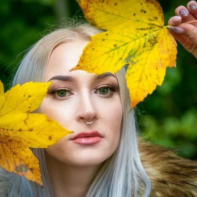 Herbst Fotoshooting in Arnsberg: Jungen Frau mit langen, blonden Haaren, hält gelbes Herbstlaub als Rahmen vor ihrem Gesicht