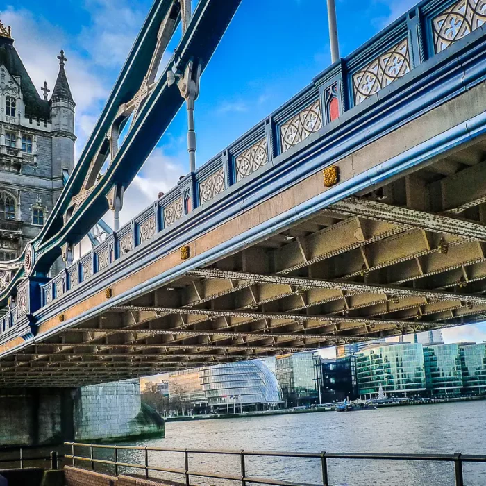 Tower Bridge in London aus niedriger Perspektive mit Stahlträgern im Vordergrund und Themse sowie moderner Skyline im Hintergrund