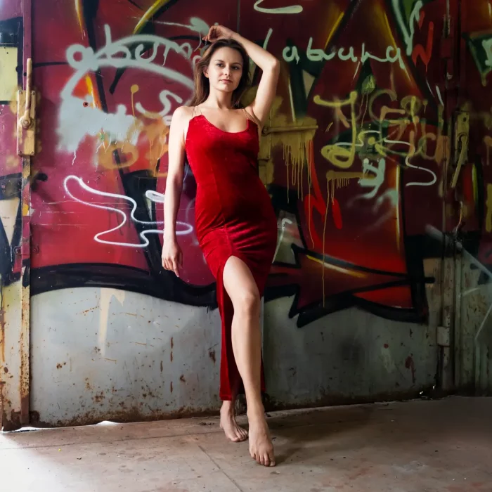Lost Place Portraitfotografie eines weiblichen Models in rotem Kleid mit Beinschlitz vor metallischem Tor mit bunter Graffiti-Bemalung in Lippstadt