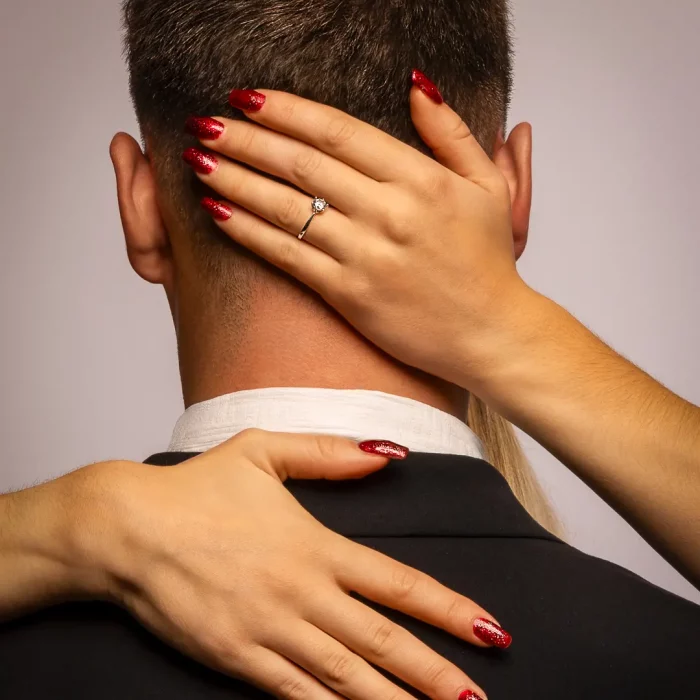 Frauenhände mit rotem Nagellack und Ring umschließen den Nacken eines Mannes im Anzug, Portraitfotografie, sinnliches Paarshooting.