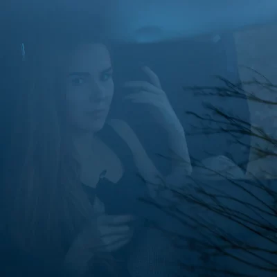 Junge Frau mit langem Haar im Auto, fotografiert durch die Windschutzscheibe – atmosphärische Innenaufnahme