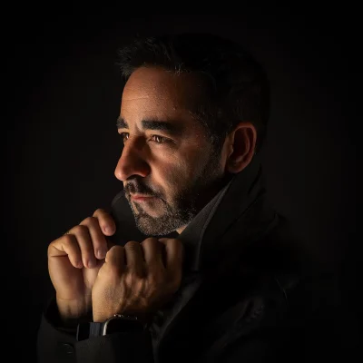 Lowkey-Profilporträt von Nevio im dunklen Mantel, dramatisches Seitenlicht vor schwarzem Hintergrund.