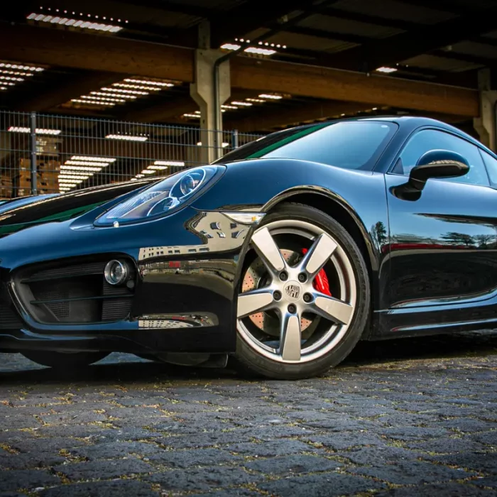 Schwarzer Porsche Cayman 981 S in seitlicher Nahaufnahme mit Betonung der glänzenden Fahrzeuglinie und silbernen Alufelgen