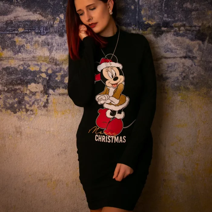 Frau mit roten Haaren, die in einem schwarzen Minnie-Maus-Weihnachtspullover entspannt an einer strukturierten Wand lehnt