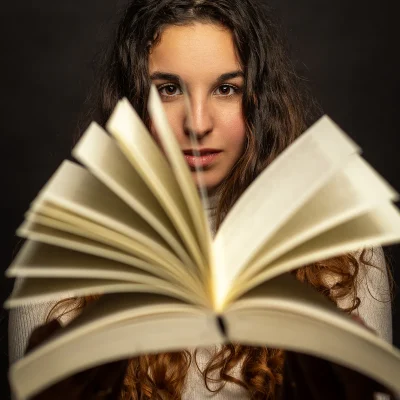Kreatives Fotoshooting: Junge Frau mit langen, lockigen Haaren, die ein aufgeschlagenes Buch in den Händen hält und direkt in die Kamera blickt.