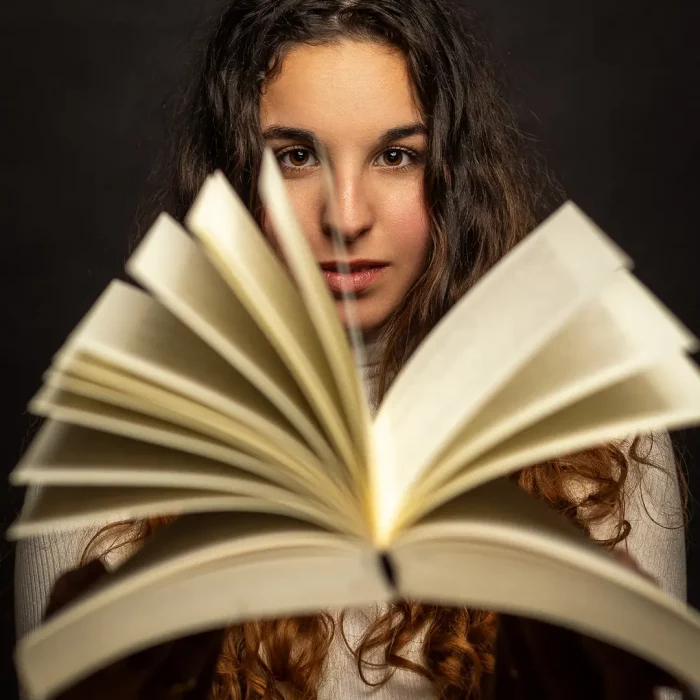 Kreatives Fotoshooting: Junge Frau mit langen, lockigen Haaren, die ein aufgeschlagenes Buch in den Händen hält und direkt in die Kamera blickt.