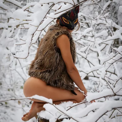 Frau mit Fuchs Maske kniet auf einem Baumstamm