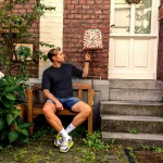 Porträtshooting mit Stefan Woischner auf einer Holzbank vor einer Backsteinfassade, neben einer karierten Stehlampe und einer Haustür