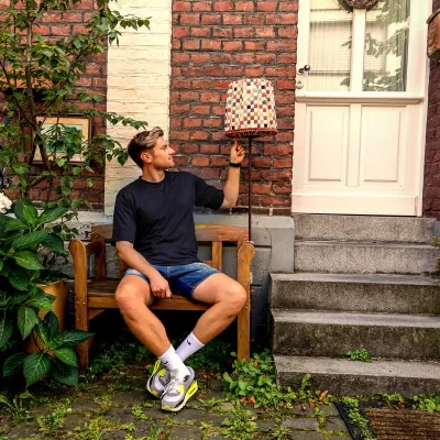 Porträtshooting mit Stefan Woischner auf einer Holzbank vor einer Backsteinfassade, neben einer karierten Stehlampe und einer Haustür