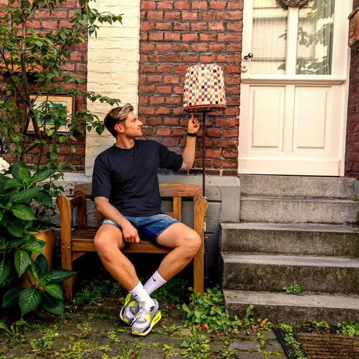 Portraitshooting mit Stefan Woischner auf einer Holzbank vor einer Backsteinfassade, neben einer karierten Stehlampe und einer Haustür