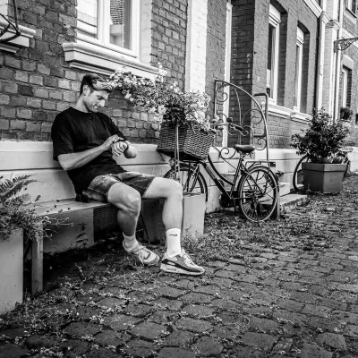 Porträtfotografie eines Mannes in sportlicher Kleidung auf einer Bank vor Backsteinfassade und Fahrrad in Soest, schwarz-weiß aufgenommen.