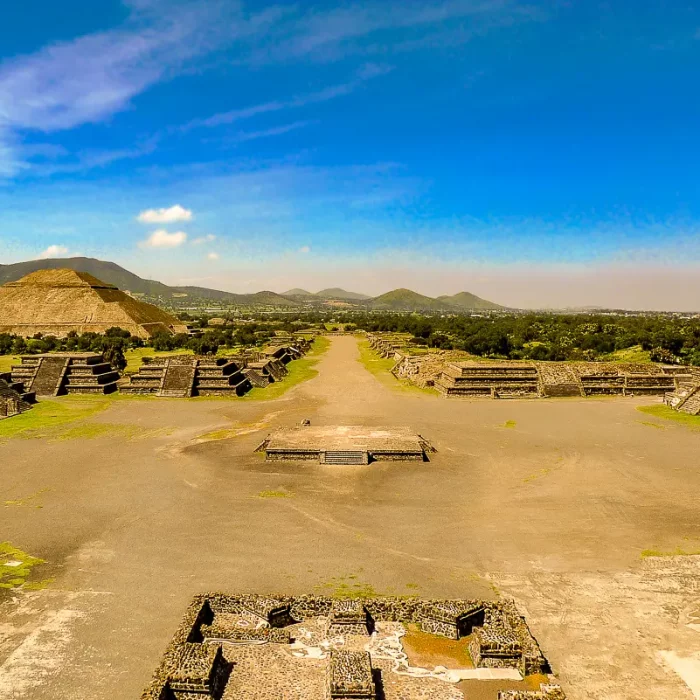Sonnenpyramide in Teotihuacan mit umliegenden Ruinen und einer breiten zentralen Straße unter blauem Himmel