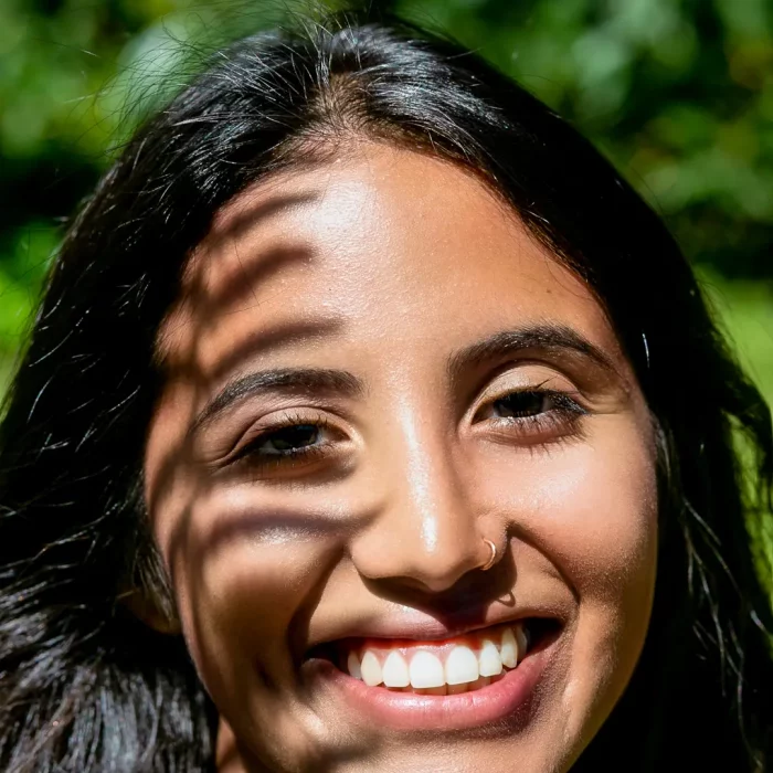 Portraitaufnahme einer lächelnden jungen Frau, Farnschattenmuster auf Gesicht, natürliche Lichtstimmung, Outdoor-Portraitfotografie