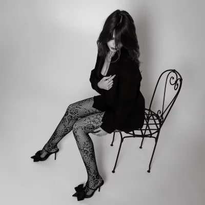 TFP-Model Valeriia in einem schwarzen Blazer, gemusterter Strumpfhose und passenden Schuhen, die auf einem dekorativen Metallstuhl sitzt.