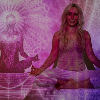 Weibliches Model mit langen, blonden Haaren in Meditationspose auf lilafarbenem Untergrund, im Hintergrund Yoga-Schattenfigur