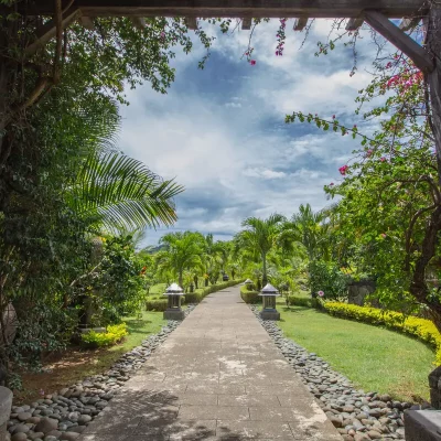 Weg mit Steinplatten, tropischen Pflanzen und Palmen durch einen gepflegten Park auf Mauritius, im Vordergrund hölzerner Durchgang