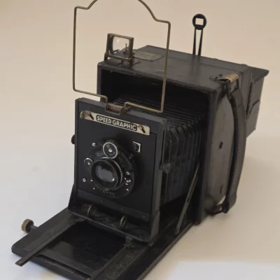 Eine schwarze Graflex Speed Graphic 4x5 Feldkamera mit ausgeklapptem Balgen und Draht-Sucher. Das Innere wurde mit einem Raspberry Pi als Digitalkamera nachgerüstet.